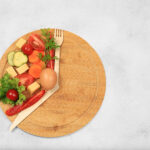 Plate with vegetables on one-third and a set of forks and knives to mimic the hands of a clock for intermittent fasting