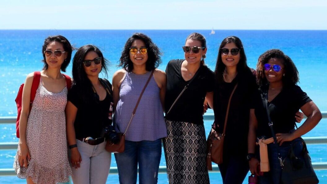 Group of women standing together on a bridge by the sea.