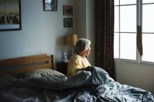 Older person in bed looking out of her window