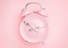 Alarm clock and plate with cutlery . Concept of intermittent fasting, lunchtime, diet and weight loss
