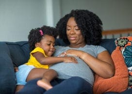 Pregnant African American mother and daughter smiling at home.