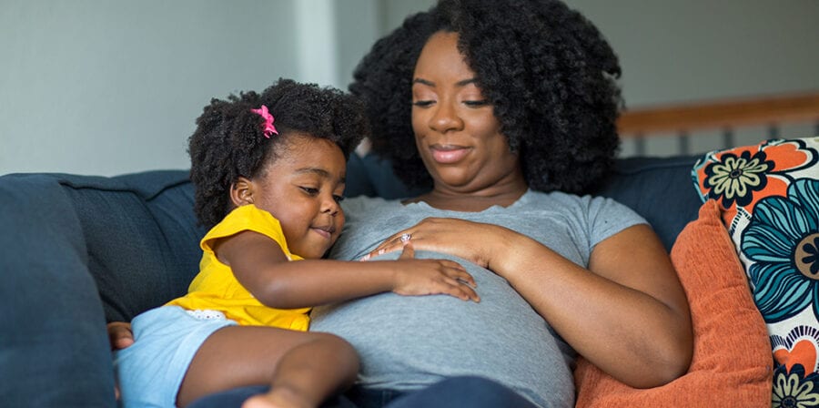 Pregnant African American mother and daughter smiling at home.