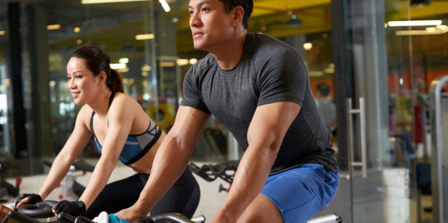 Sporty Asian couple riding stationary bicycles while having intensive workout at modern gym, group portrait (DragonImages/iStockphoto)