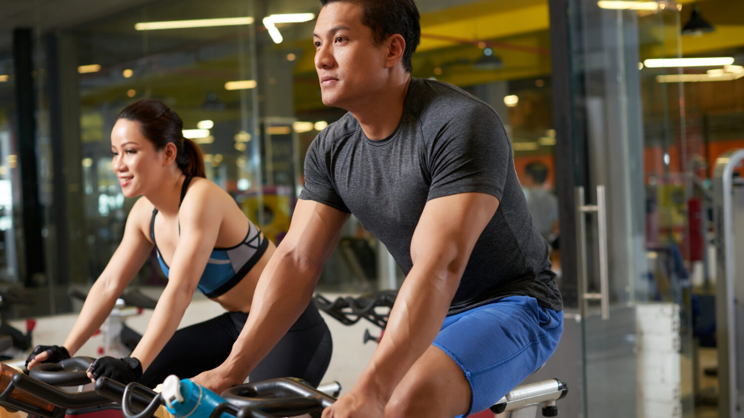 Sporty Asian couple riding stationary bicycles while having intensive workout at modern gym, group portrait (DragonImages/iStockphoto)