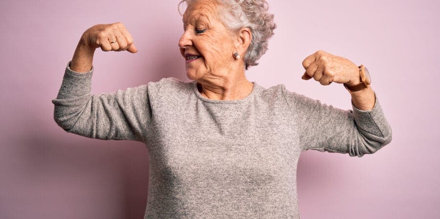 Senior beautiful woman wearing casual t-shirt standing over isolated pink background showing arms muscles smiling proud. Fitness concept. Aaron Amat/iStock