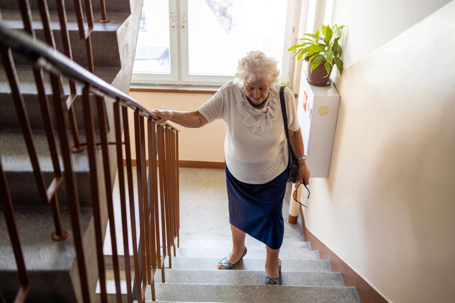 Older woman holding the handrails and walking up the stairs