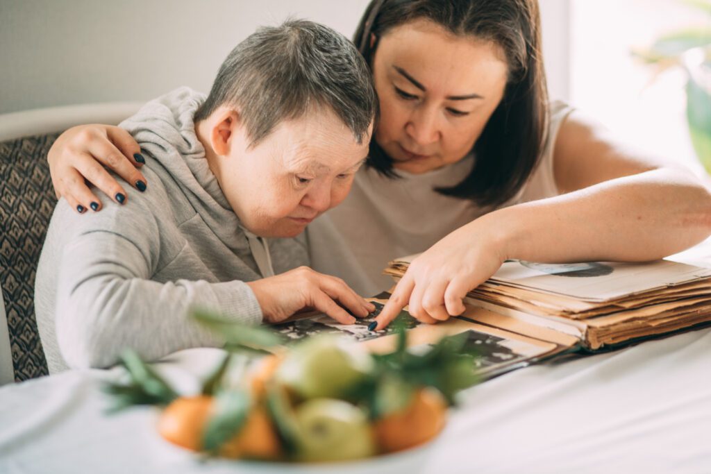 Asian woman points a elderly woman with Down syndrome to a photo in an old album